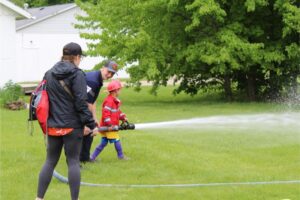 Child spraying water with firefighter assistance