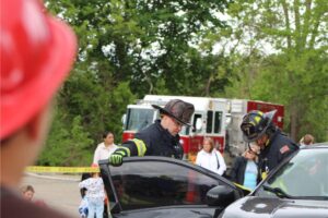Firefighters examine a car at an outdoor scene.